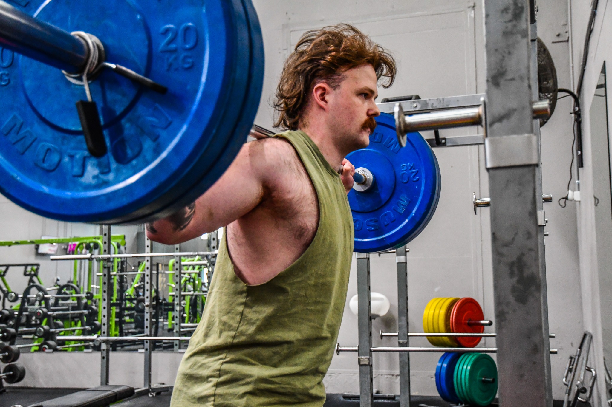 A gym member standing with a barbell across his upper back in a squat rack