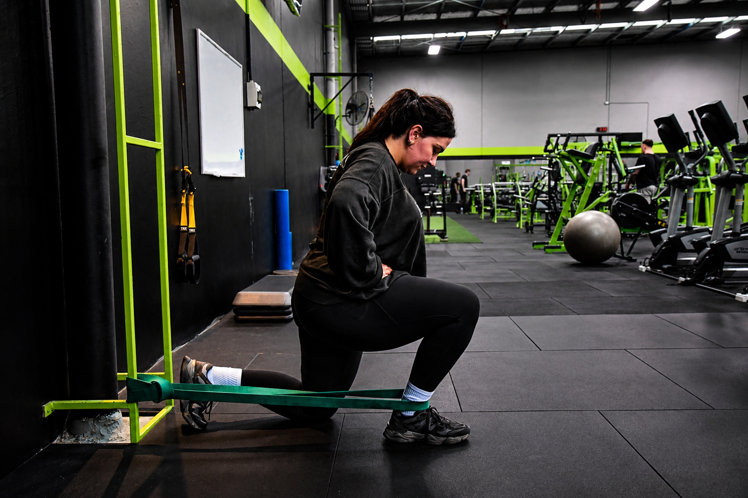 Athlete practising a half-kneeling band-assisted ankle mobility movement in the gym